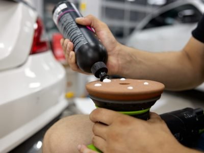 Man car service worker applying wax cream on disk of polisher machine. Transport maintenance workshop, carwash garage. Closeup view